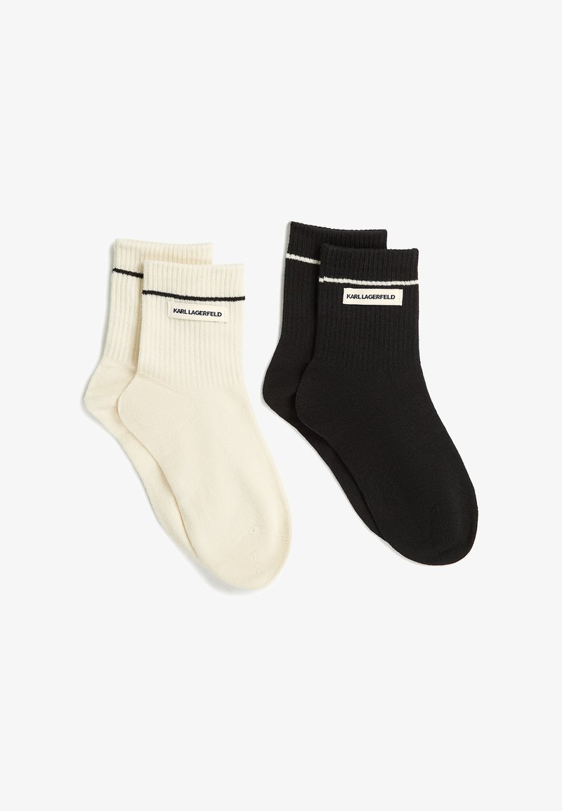 To par ribstrikkede sokker, en sort og en hvid, begge med en tynd stribe nær toppen og en "Karl Lagerfeld" label på kanten.