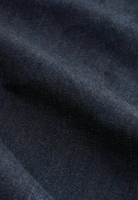 Tmavý denim s jemným leskem, charakterizovaný hladkou texturou a jemným tkaním. Barva je tmavě námořnická modř s lehkým odleskem světla.