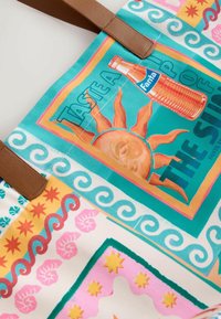 Sac fourre-tout coloré avec illustration de soleil, une bouteille vintage de Fanta, motifs ondulés, étoiles décoratives et motifs coquillages, avec des anses marron.