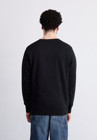 Sudadera negra de manga larga y cuello redondo. Presenta una textura suave y puños ajustados, combinada con unos pantalones vaqueros azules sueltos.