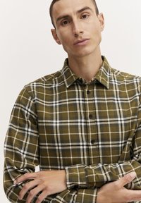 Grøn og beige ternet skjorte lavet af flannel, med en knappet krave og sorte knapper, med lange ærmer, vist på en model.