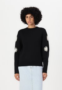 Svart genser med lange ermer, prydet med hvite broderte tusenfryd på armene. Laget av mykt materiale, med rund halslinning og tettsittende midje.