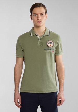Polo shirt verde oliva con colletto a contrasto, patch ricamato, maniche corte e dettagli di cucitura discreti. Materiale di cotone liscio.