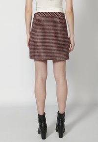 Jupe mini à carreaux rouges avec une coupe ajustée, dotée d'une taille lisse et de poches discrètes. À associer avec des bottines noires.