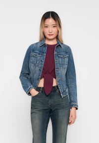 Denimjakke med to brystlommer, lys blå farge, klassisk design, kombinert med en burgunder knyttet skjorte og mørkeblå jeans.
