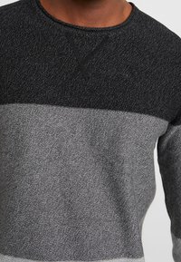 Grauer und schwarzer Langarmpullover mit strukturiertem Strick, der ein horizontales Farbschema und einen runden Halsausschnitt aufweist.