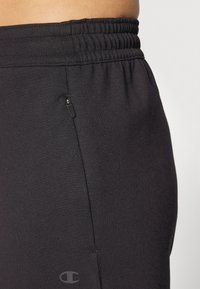 Black athletic pants made of soft fabric with an elastic waistband, featuring a zippered pocket on the side and a subtle logo.