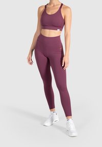 Bordo urheiluliivihihna ja korkeat legginsit joustavasta kankaasta. Valkoiset lenkkarit hienovaraisilla brändeillä täydentävät urheilullista ilmettä.