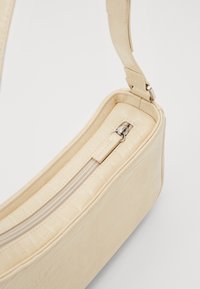 Pochette zippée en simili cuir crème doux avec embossage crocodile, dotée d'une fermeture éclair et d'une bandoulière réglable. Forme rectangulaire compacte.