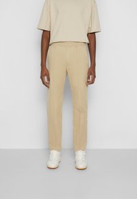 Pantalon beige avec une taille élastique, coupe droite et coutures minimales ; associé avec un haut beige à manches courtes et des baskets blanches.