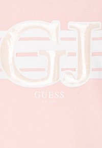 Sudadera de algodón de color rosa claro con gran logo blanco brillante "GJ" y rayas horizontales blancas. Incluye el nombre de la marca "GUESS" y "EST. 1981" debajo.