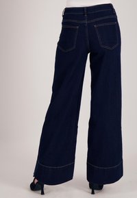 Wijde donkerblauwe jeans met hoge taille, voorzien van twee zakken aan de achterkant en contrasterende gele stiksels langs de naden.