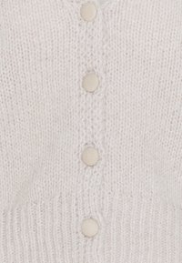 Cárdigan beige claro de punto con escote en V, con cinco botones redondos y texturizados y ribete acanalado. Textura suave y acogedora que aporta calidez.