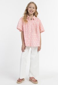 Camicia a maniche corte, con bottoni, di colore rosa con motivo a foglie, abbinata a pantaloni bianchi a gamba larga e sandali espadrillas rosa.