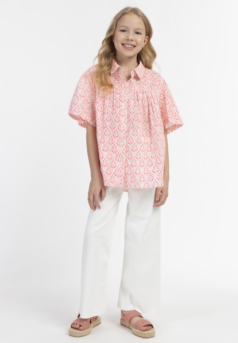Camicia a maniche corte, con bottoni, di colore rosa con motivo a foglie, abbinata a pantaloni bianchi a gamba larga e sandali espadrillas rosa.