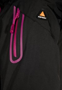 Giacca nera con una zip e rifiniture viola in evidenza. Presenta un logo del marchio arancione e nero sulla spalla. Dettaglio in tessuto texture.