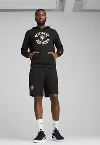 Sort hættetrøje og shorts med ordet "Portugal" i hvid, rød skildredetalje, med Puma-logo. Materialet ser blødt og afslappet ud.