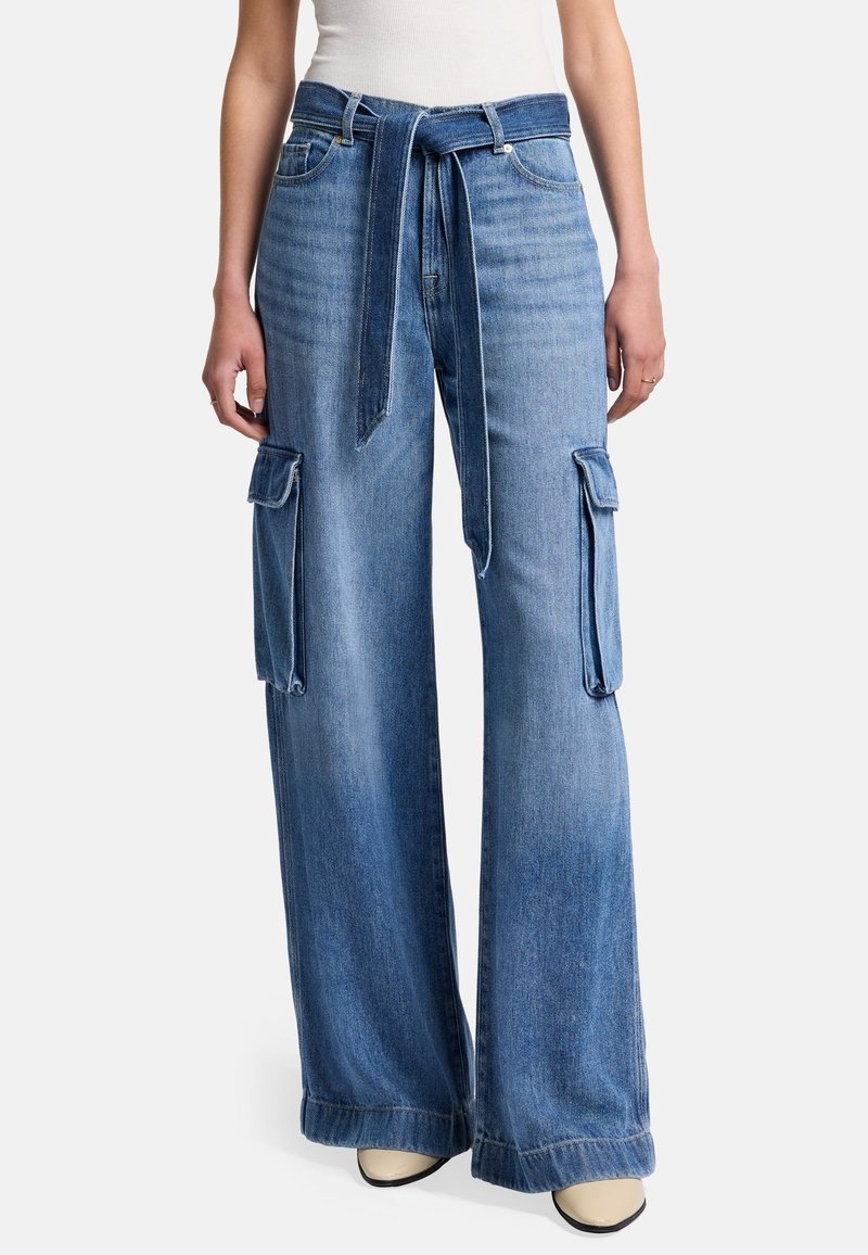 Pantalons cargo en denim à jambes larges avec une taille ceinturée, teinte bleu clair, deux grandes poches latérales et détails à ourlet brut.