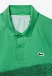 Grön polo t-shirt med en gradientdesign, slät textur, tre knappar och en liten broderad logotyp på vänster bröst.