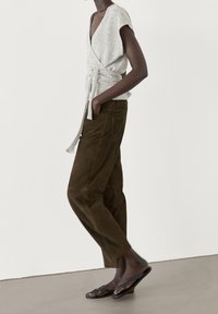 Gray, textured wrap top with short sleeves and tie detail, paired with dark green corduroy pants. Flat black sandals complete the outfit.