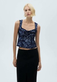 Námornícky modrý crop top so flitrami a štvorcovým výstrihom, s ramienkami, v kombinácii s čiernou sukňou s vysokým pásom a predným rozparkom.