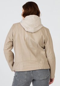 Beige läderjacka med en mjuk, ljus hoodie fäst, med sömmar och subtila accenter, i kombination med grå denim.