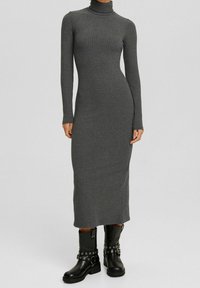 Abito grigio a coste lungo e aderente con collo alto e maniche lunghe, abbinato a stivaletti neri alla caviglia con hardware decorativo.
