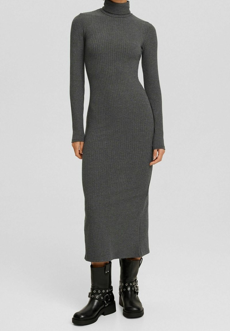 Abito grigio a coste lungo e aderente con collo alto e maniche lunghe, abbinato a stivaletti neri alla caviglia con hardware decorativo.