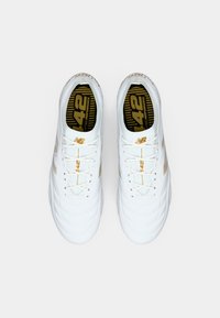 Os ténis brancos desportivos apresentam uma textura suave, detalhes dourados, um design com atacadores e um logótipo na palmilha com "42" em preto e dourado.