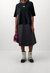 Musta t-paita valkoisella logolla, tikkikuosiset tummanharmaat hame, kiiltävä vaaleanpunainen käsilaukku ja vaaleat eristetyt saappaat.