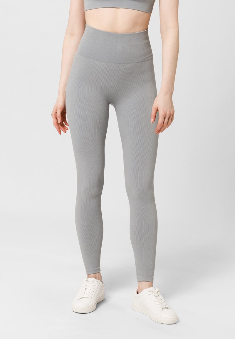 Leggings grigi ribattuti con vita alta, caratterizzati da una texture liscia e un design aderente. Abbinati a sneaker bianche.
