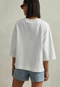 Hvid oversized t-shirt med korte ærmer, lavet af blødt stof. Matchet med lyseblå denim shorts med opkrøllet kant.