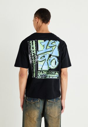 Musta puuvillapaita, jossa on eläväinen graafinen printti sinisenä ja vihreänä selkäpuolella, tekstiä ja ikoneita, rento malli, lyhyet hihat.