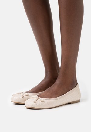 Beżowe płaskie buty o teksturowanym wykończeniu, zaokrąglonym nosie i związanym sznurku z przodu. Wykonane z miękkiego materiału o minimalistycznym designie.