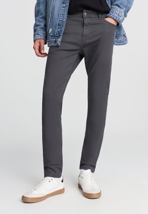 Jeans in cotone grigio con design slim fit, cinque tasche e chiusura con bottone. Abbinati a scarpe da ginnastica bianche e una giacca di jeans.