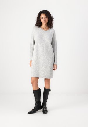 Abito grigio in maglia con una texture a coste, caratterizzato da un motivo geometrico. Indossato con stivali in pelle nera al ginocchio e punta affusolata.
