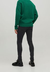 Suéter verde texturizado con un dobladillo acanalado, combinado con jeans negros ajustados y botas negras de cordones, visto desde la parte posterior.