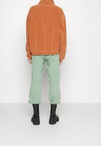 Kurtka ze sztruksu w kolorze rdzy o luźnym kroju, zestawiona z miętowozielonymi spodniami dresowymi. Modelka nosi czarne botki na masywnej podeszwie.