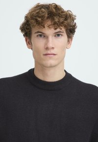 Maglione grigio scuro con colletto rotondo a coste. Texture morbida, design semplice, senza motivi o decorazioni visibili.