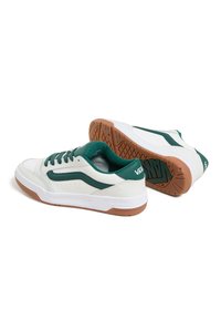 Weiße Sneakers mit grünen Akzenten, ausgestattet mit einem Obermaterial aus Leder und Textil, Belüftungsöffnungen und einer braunen Gummisohle mit strukturiertem Profil.