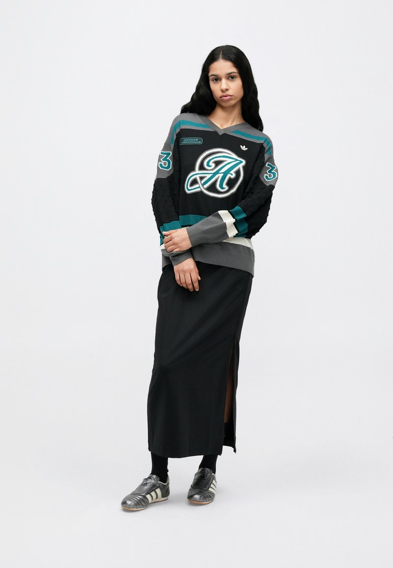 Maillot de sport noir avec des accents turquoise, gris et blanc, présentant un grand logo et un numéro. Porté avec une jupe longue noire, assorti à des baskets argentées.