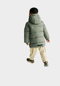 Grønne pufferjakke med hætte, som har vandret syninger og et logo-patch ved sømmen. Bæres med cremede cargo-bukser og mørke sneakers.