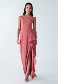 Abito lungo in tessuto rosa tenue, con design asimmetrico a una spalla, dettaglio laterale con volant e spacco alto sulla coscia.