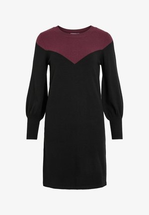 Svart strikket kjole med en mørkerød trekantet innsats, rund hals, og lange puffede ermer. Ribbestrikkede mansjetter og glatt tekstur.