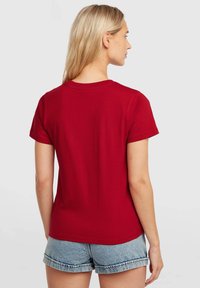 Red cotton t-shirt with short sleeves, round neckline, and a relaxed fit, paired with light blue denim shorts. No patterns or accents.