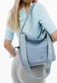 Sac en tissu bleu doux avec une bandoulière tressée et une quincaillerie en argent. Présente une forme décontractée et un logo embossé, conçu pour un usage quotidien.