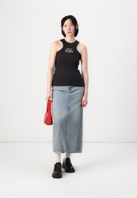 Zwarte geribbelde mouwloze top met wit logo, gecombineerd met een lange spijkerrok, zwarte platform schoenen en een kleine rode handtas.