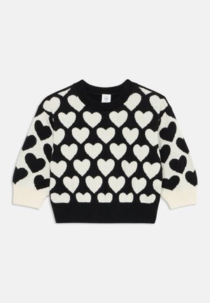 Suéter negro con un gran patrón de corazones blancos; cuello redondo y puños acanalados; textura de punto suave. Etiqueta de la marca visible en el cuello.