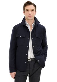 Giacca blu navy realizzata in tessuto con colletto strutturato e due tasche sul petto, caratterizzata da bottoni a pressione in tonalità argentata e vestibilità su misura.