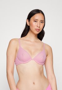 Sutiã rosa de tecido ribado com copas triangulares, alças finas e aros. Apresenta um design sem costuras para uma aparência suave.